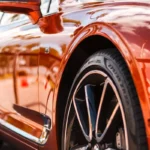 A clean, polished car parked outside a detailing shop. The car gleams under the sunlight, reflecting the surrounding environment.