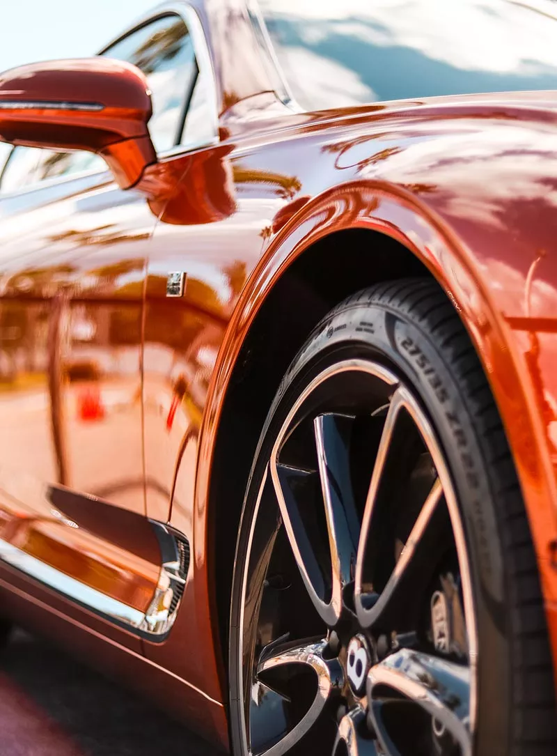 A clean, polished car parked outside a detailing shop. The car gleams under the sunlight, reflecting the surrounding environment.